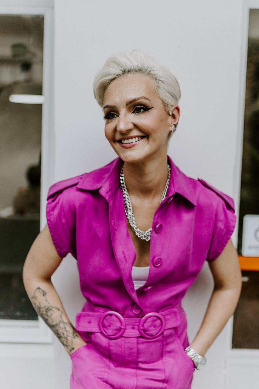Gabi Rampi sorrindo, vestindo um look rosa vibrante